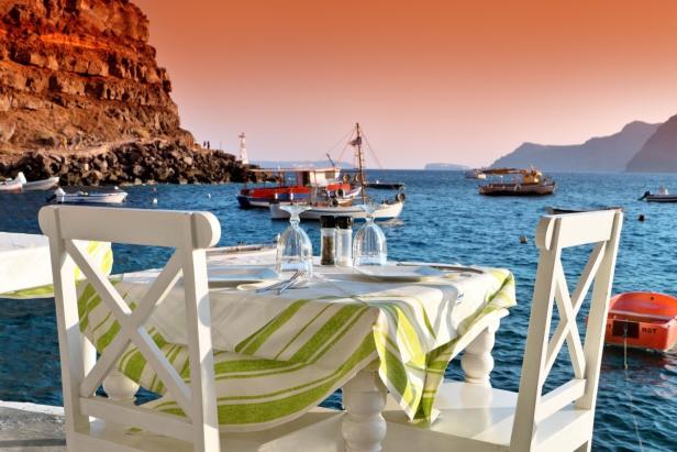 Ein gedeckter Tisch mit Blick auf das Meer und Fischerboote bei Sonnenuntergang.