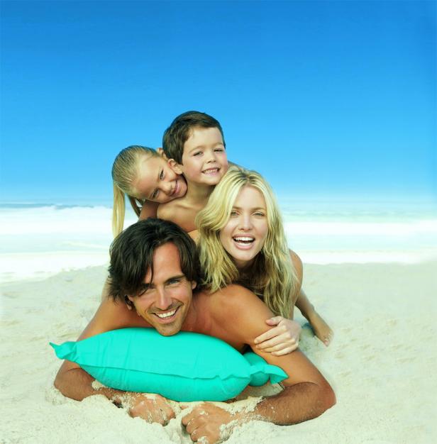 Eine glückliche Familie liegt am Strand übereinander gestapelt.