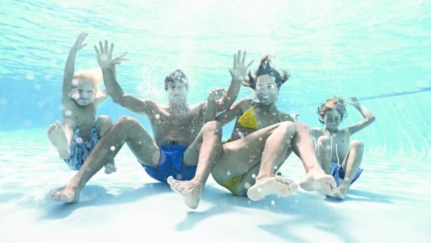 Eine Familie schwimmt und spielt unter Wasser in einem Schwimmbad.