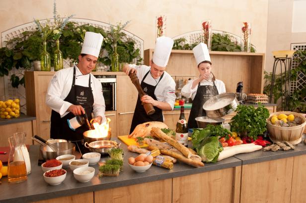 Drei Köche bereiten in einer Küche verschiedene Speisen zu.