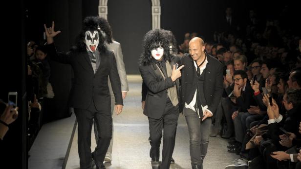 Männer in Anzügen und mit KISS-Make-up laufen auf einem Laufsteg an einem Publikum vorbei.