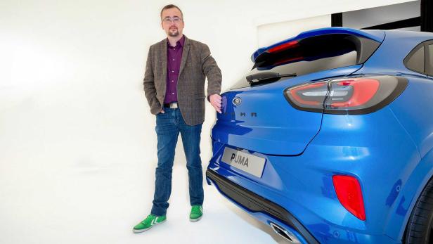 Ein Mann steht neben einem blauen Ford Puma.