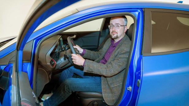 Ein Mann mit Brille sitzt in einem blauen Auto am Steuer.