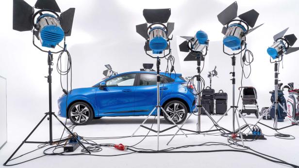Ein blaues Auto steht in einem Fotostudio, umgeben von Scheinwerfern und Zubehör.