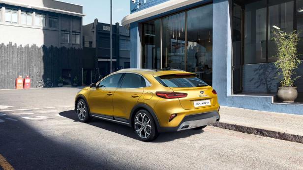 Ein goldfarbener Kia XCeed parkt vor einem Gebäude in einer städtischen Umgebung.