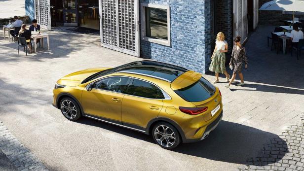 Ein goldener Kia XCeed steht vor einem Café, an dem zwei Frauen vorbeigehen.