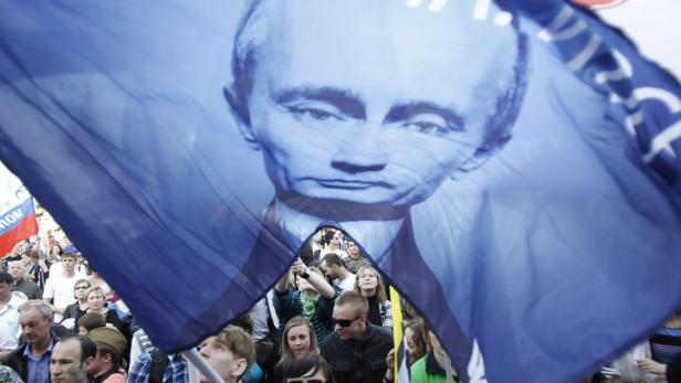 Eine Menschenmenge mit einer blauen Fahne, die ein Porträt von Wladimir Putin zeigt.