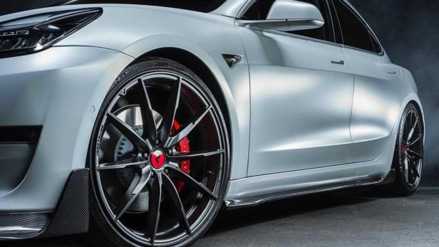 Ein silbernes Tesla Model 3 mit schwarzen Felgen und roten Bremssätteln.