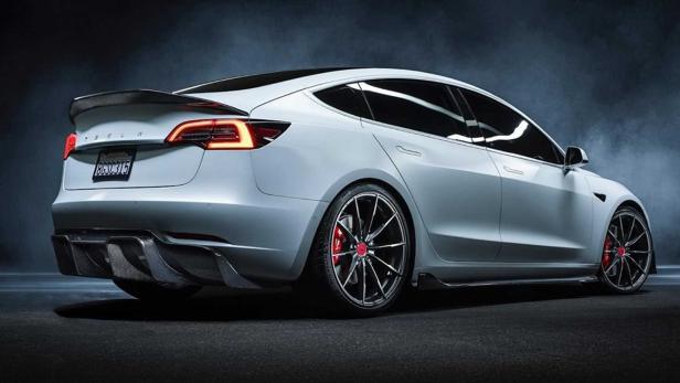 Ein weißes Tesla Model 3 mit Heckspoiler und roten Bremssätteln.