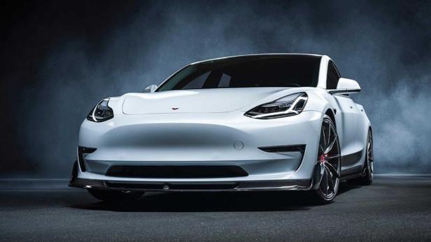 Ein weißes Tesla Model 3 mit sportlichen Modifikationen vor einem dunklen Hintergrund.