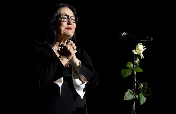 Eine Frau mit Brille steht neben einem Mikrofonständer mit einer weißen Rose.