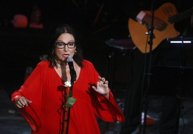 Eine Sängerin mit Brille und rotem Kleid singt mit einem Mikrofon in der Hand.