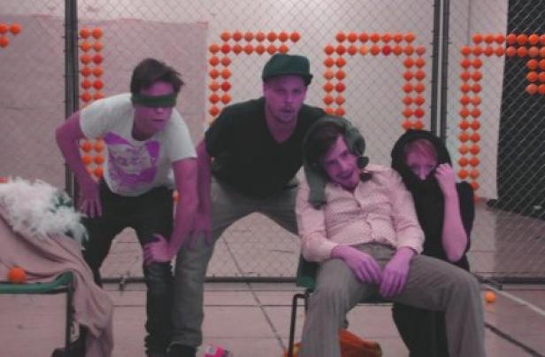 Eine Gruppe von vier Personen posiert vor einem Gitter, das mit orangen Bällen dekoriert ist.