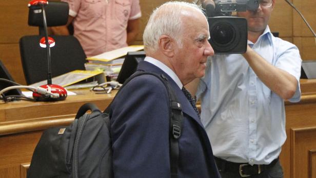 Ein älterer Mann mit Anzug und Rucksack wird von einem Kameramann gefilmt.