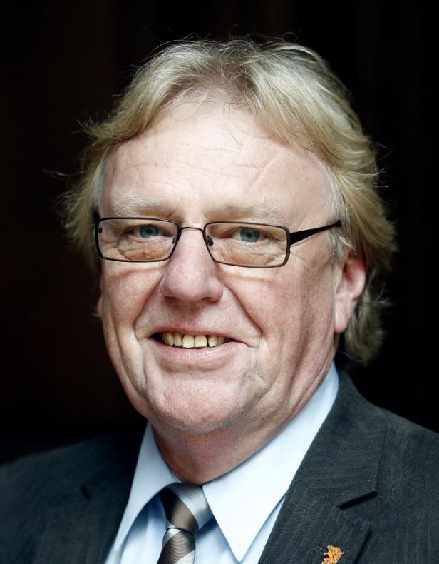 Ein Mann mit Brille und Anzug lächelt in die Kamera.