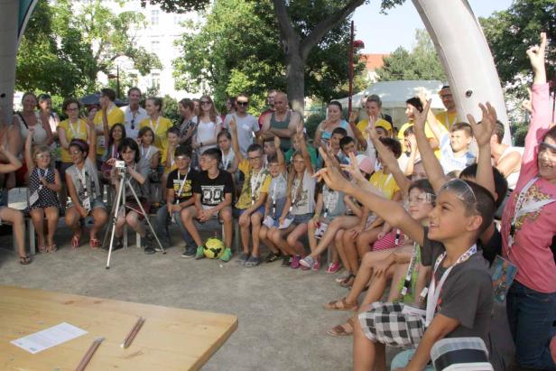 Eine Gruppe Kinder sitzt draußen und hebt die Hände.