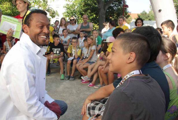 Ein Mann im weißen Kittel spricht lächelnd vor einer Gruppe von Kindern.