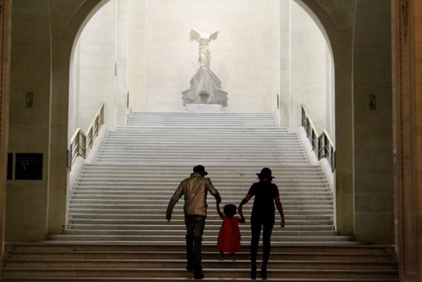 Eine Familie geht die monumentale Treppe hinauf, an deren Ende die Nike von Samothrake steht.