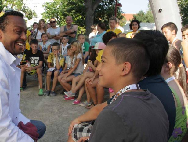 Eine Gruppe Kinder sitzt und hört einem lächelnden Mann zu.