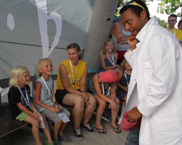 Ein Mann im weißen Kittel spricht mit einer Gruppe von Kindern.