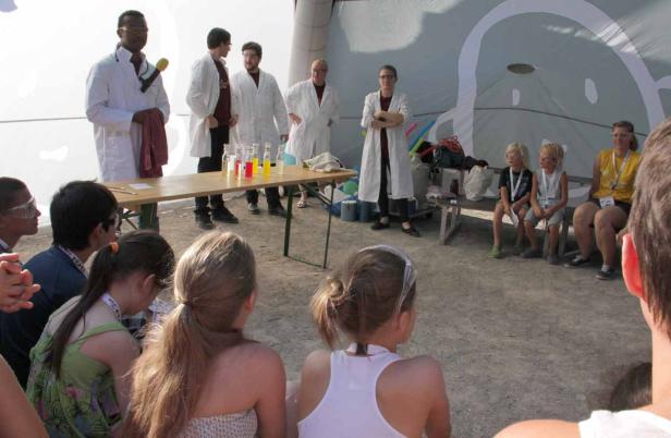 Kinder beobachten Wissenschaftler bei einem Experiment mit farbigen Flüssigkeiten.