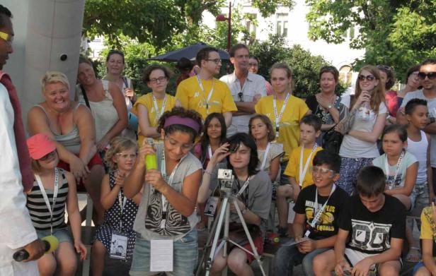 Eine Gruppe von Kindern und Erwachsenen sitzt im Freien, einige tragen gelbe T-Shirts.