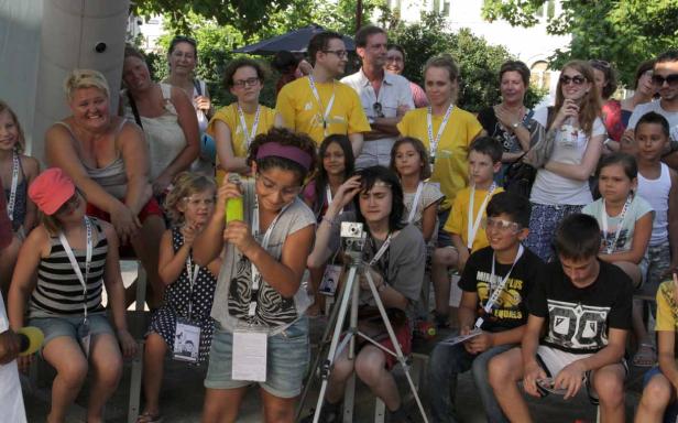 Eine Gruppe von Kindern und Erwachsenen sitzt im Freien, einige mit Kameras und Namensschildern.