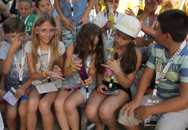 Eine Gruppe Kinder sitzt zusammen und experimentiert mit Flüssigkeiten in Flaschen.