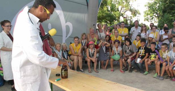 Ein Mann im Laborkittel führt vor einer Gruppe von Kindern ein Experiment mit einer Flüssigkeit durch.