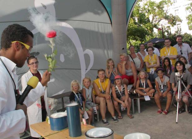 Ein Mann im Laborkittel demonstriert eine rauchende Rose vor einer Gruppe von Kindern.