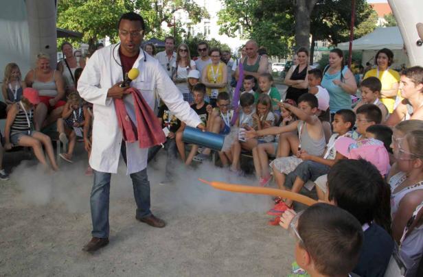 Ein Mann im Laborkittel führt ein Experiment mit Trockeneis vor einer Gruppe von Kindern durch.