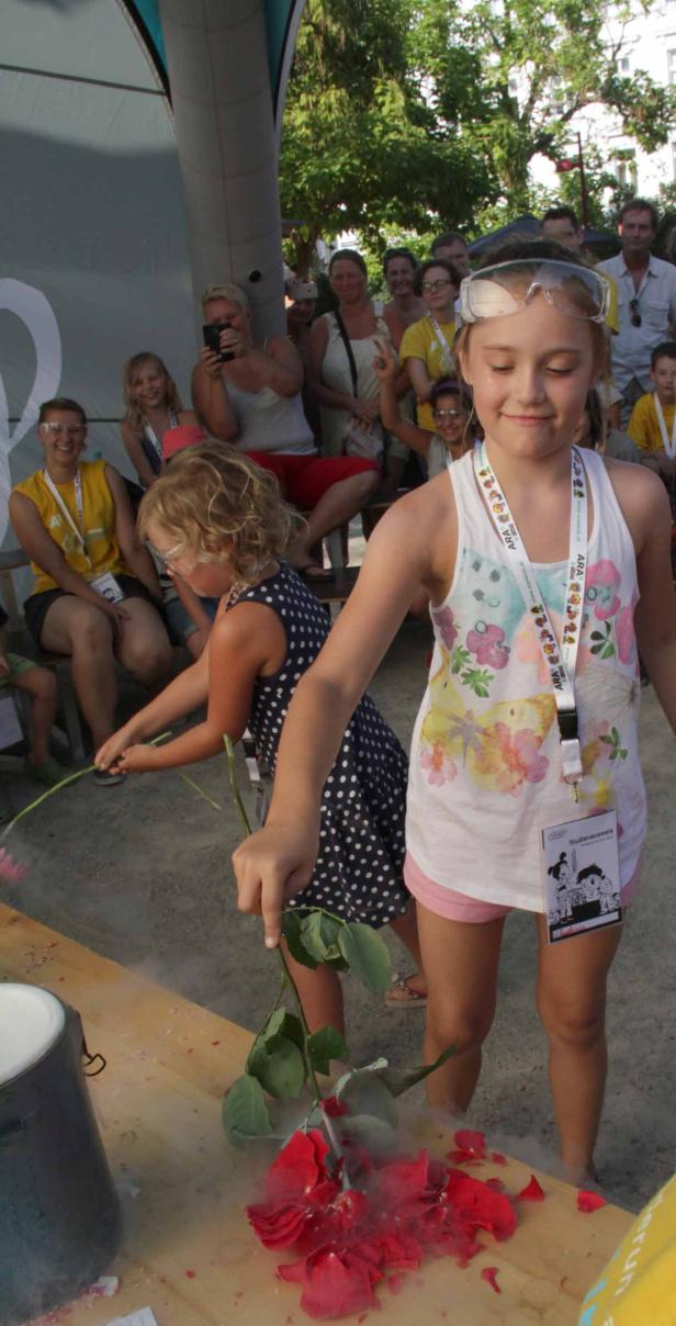 Zwei Mädchen mit Schutzbrillen tauchen Rosen in flüssigen Stickstoff, wodurch diese zerbrechen.