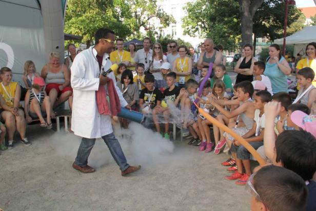 Ein Mann im Laborkittel führt ein Experiment mit Rauch vor einer Gruppe von Kindern durch.