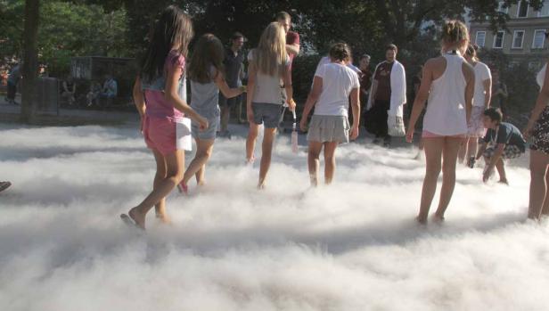 Eine Gruppe von Menschen, hauptsächlich Kinder, watet durch dichten Nebel in einem Park.