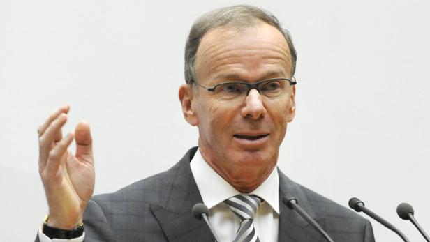 Ein Mann mit Brille gestikuliert vor mehreren Mikrofonen.