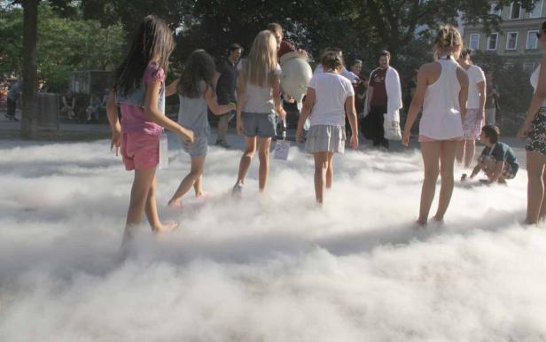 Kinder spielen barfuß in einer Nebelinstallation im Freien.