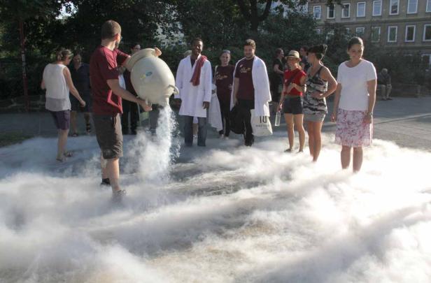 Eine Gruppe von Menschen steht in einer Wolke aus Trockeneis, während eine Person Trockeneis aus einem Gefäß gießt.