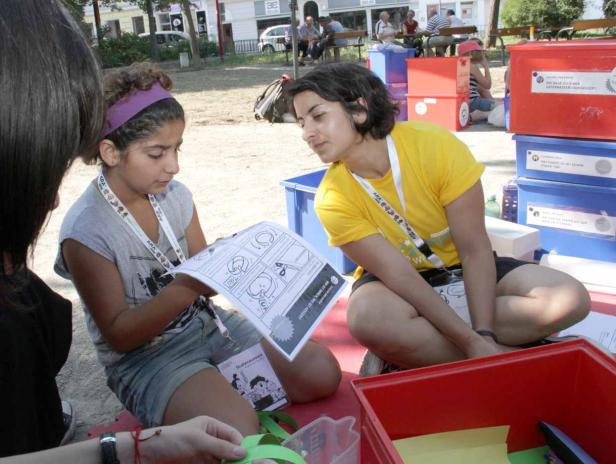 Zwei junge Frauen sitzen im Freien und betrachten ein Comic-Heft.