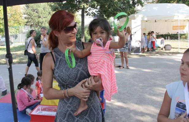 Eine Frau hält ein kleines Mädchen mit Schnuller auf dem Arm, beide halten grüne Armreifen hoch.