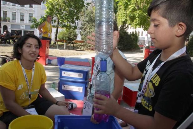 Ein Junge führt ein Experiment mit zwei Plastikflaschen und einer Frau im Park durch.