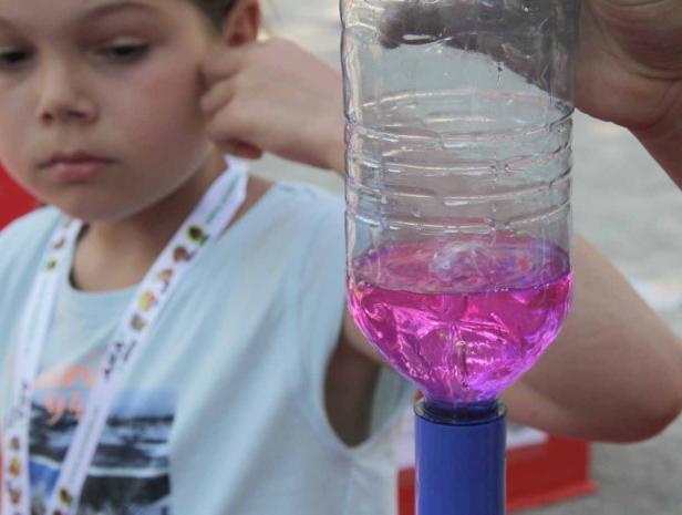 Ein Mädchen betrachtet eine Plastikflasche mit pinkfarbener Flüssigkeit und einem kleinen Tornado darin.