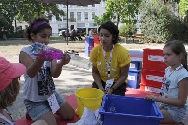 Kinder experimentieren mit Wasser und Plastikflaschen im Freien.