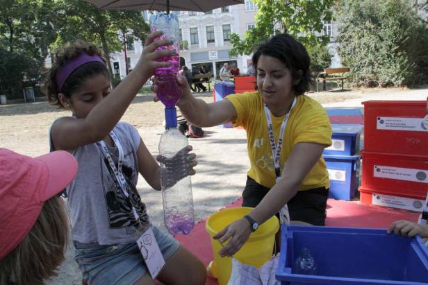 Zwei Mädchen experimentieren mit zwei durch einen Adapter verbundenen Wasserflaschen.