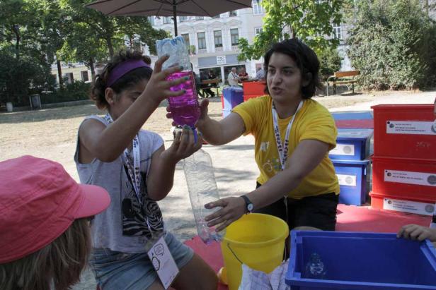 Eine Frau zeigt einem Mädchen, wie man Wasser in eine Plastikflasche füllt.