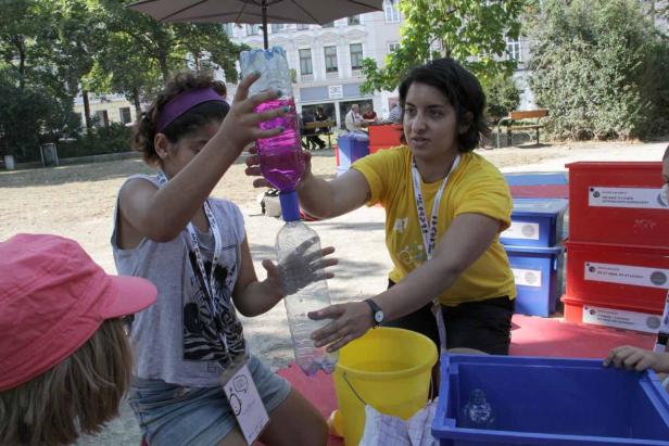 Zwei Frauen führen ein Experiment mit zwei Plastikflaschen und farbigem Wasser im Freien durch.