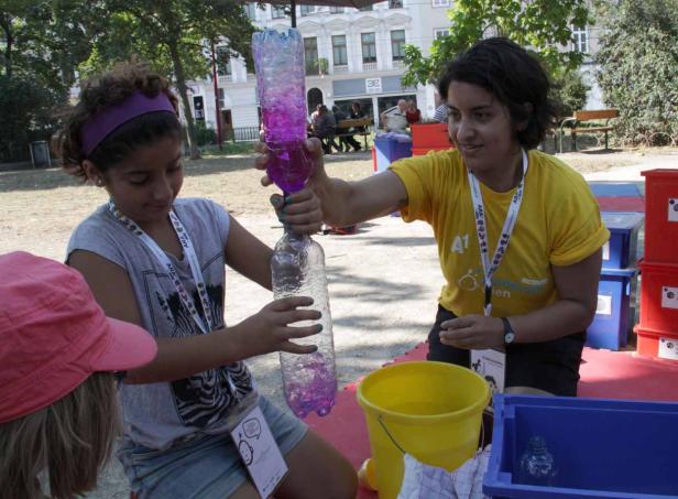 Ein Mädchen und eine Frau halten zwei verbundene Plastikflaschen mit farbiger Flüssigkeit.