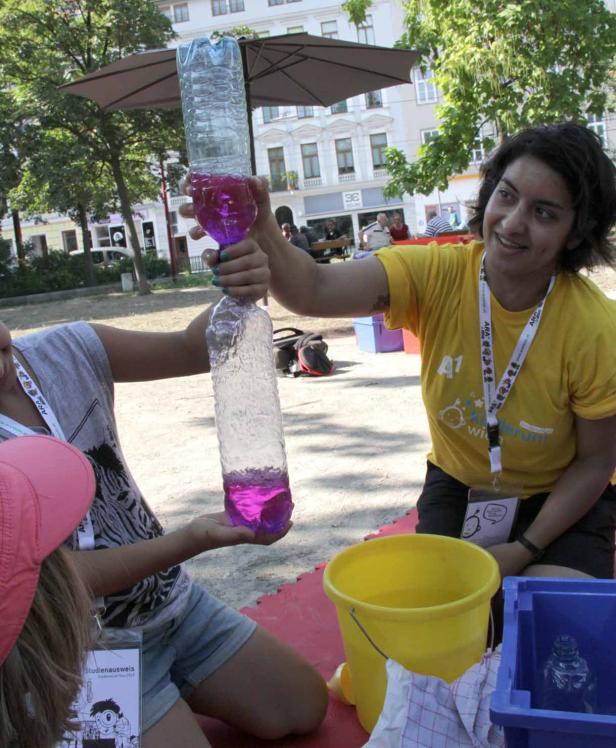 Zwei Frauen demonstrieren einen Wasserwirbel in zwei Plastikflaschen.