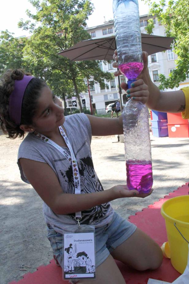 Ein Mädchen hält zwei verbundene Plastikflaschen mit pinkfarbenem Wasser in der Hand.