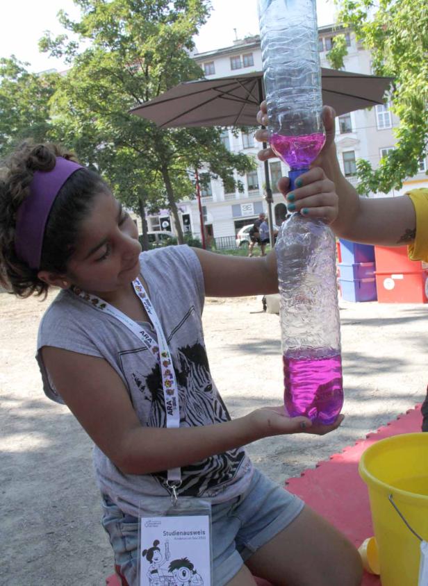 Ein Mädchen hält zwei verbundene Plastikflaschen mit pinkfarbener Flüssigkeit.