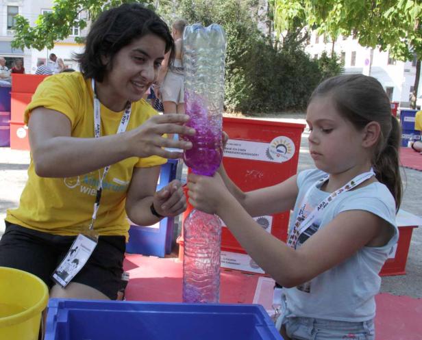 Eine Frau und ein Mädchen hantieren mit zwei Plastikflaschen, die mit farbiger Flüssigkeit gefüllt sind.